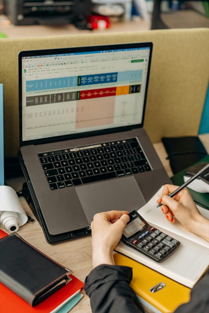 pexels photo 8296983 8296983 Hands writing notes beside a laptop displaying data in a bright office setup.